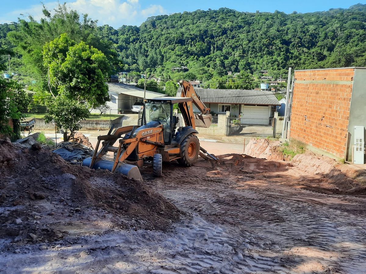 Retroescavadeira nivelando lote residencial com morro ao fundo